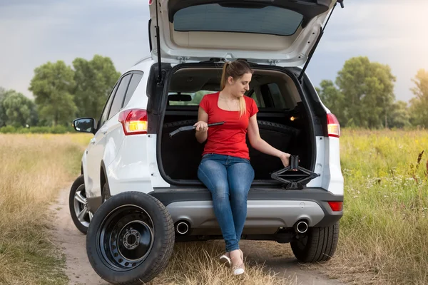 Frustrated woman sitting in broken car looking on the tools for — Stock Photo, Image