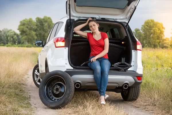 Young woman sitting in broken car at field — Stock Photo, Image