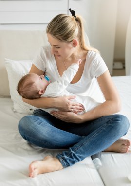 3 aylık bebek oğlu ile yatağın üstüne oturan genç anne