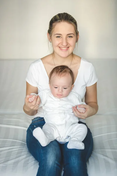 Mooie lachende moeder zittend op bed en houden haar babyjongen — Stockfoto