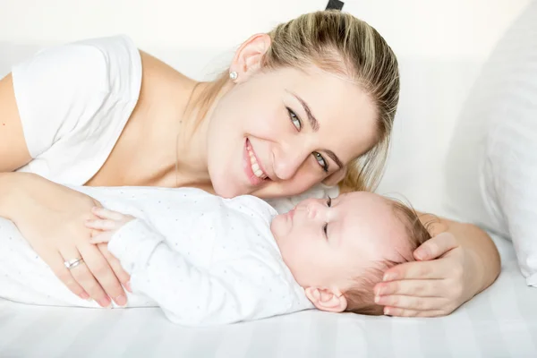 Porträt einer lächelnden Mutter, die mit ihrem 3 Monate alten Baby im Bett liegt — Stockfoto