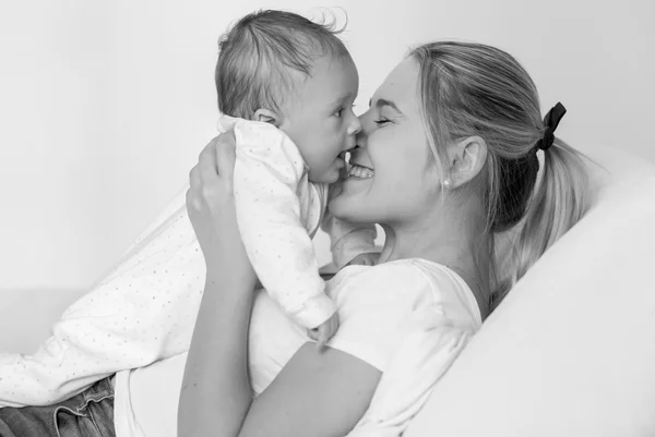 Black and white portrait of cheerful mother lying on bed and kis — Stock Photo, Image