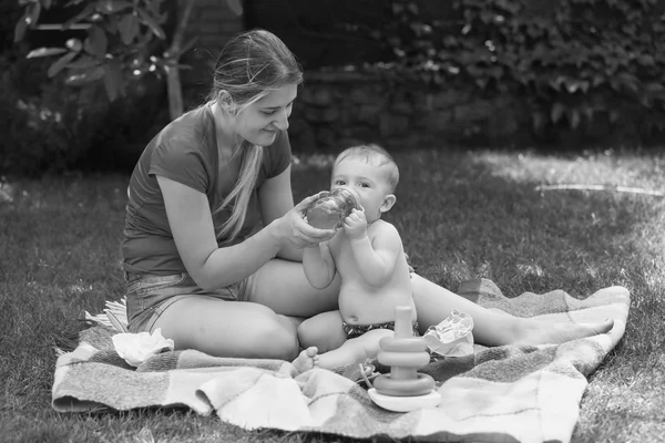Zwart-wit beeld van moeder voeden haar baby in het park — Stockfoto