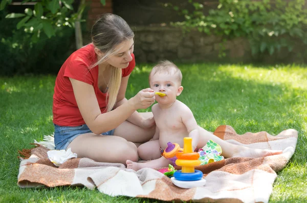 Молода мати годує свого маленького хлопчика на пікніку в парку — стокове фото