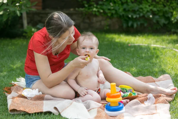 Bela mãe alimentando seu bebê menino na grama no parque — Fotografia de Stock