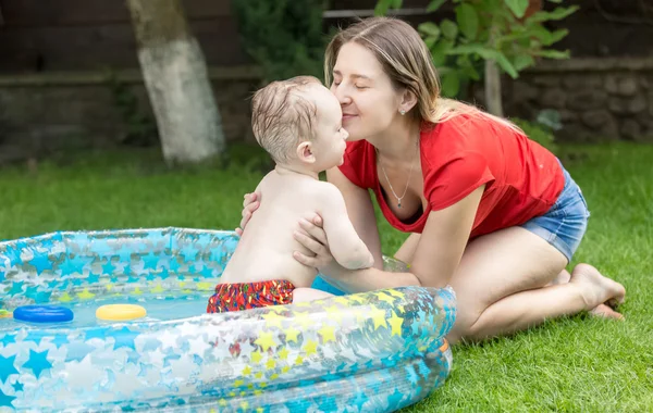 Feliz madre jugando con su bebé nadando en la piscina en el jardín —  Fotos de Stock