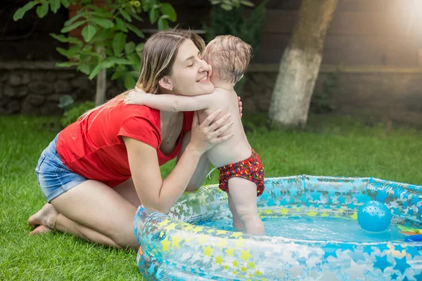 Jovem mãe abraçando seu bebê menino na piscina no jardim — Fotografia de Stock