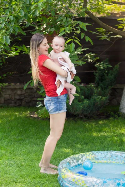 Jovem mãe levando seu bebê menino para fora da piscina inflável após sw — Fotografia de Stock