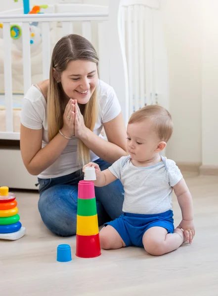 Jeune mère regardant son bébé garçon assembler pyramide jouet sur f — Photo