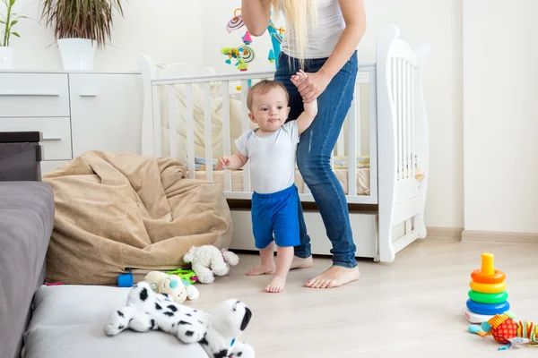 Matka trzyma chłopca przez ręce i chodzenie w salonie — Zdjęcie stockowe