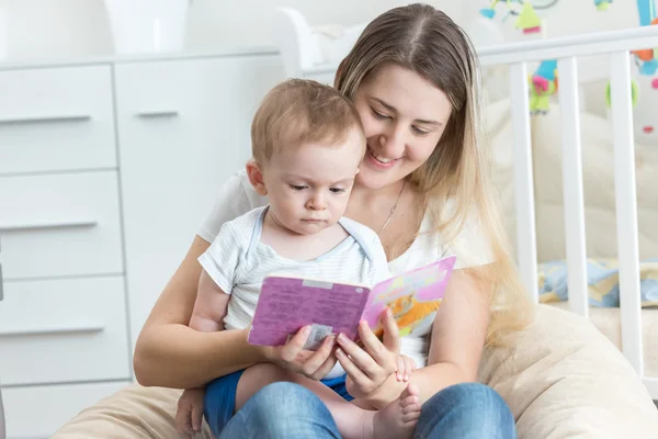 Schöne lächelnde Mutter liest ihrem 9 Monate alten Baby Buch vor — Stockfoto