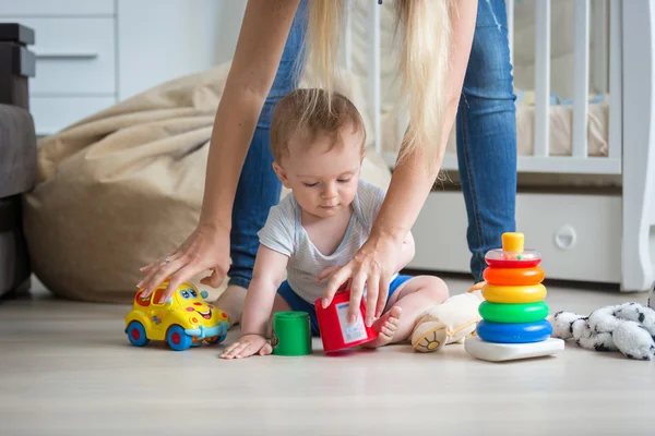 Madre che dà giocattoli al suo bambino di 10 mesi che gioca sul floo — Foto Stock