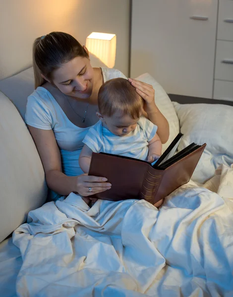 Schöne lächelnde Mutter, die ihrem kleinen Jungen Geschichte vorliest, bevor sie geht — Stockfoto