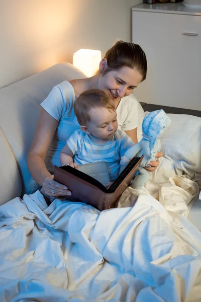 Hermosa madre sonriente leyendo libro de cuentos de hadas a su bebé en b —  Fotos de Stock