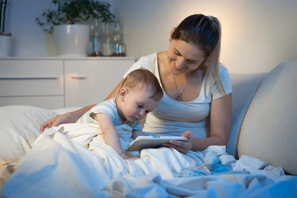 Niño sentado en la cama con la madre y el uso de la tableta digital en —  Fotos de Stock