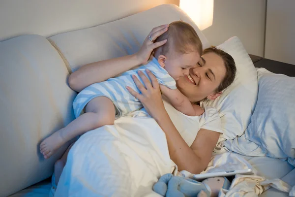 Feliz joven madre jugando y abrazando a su bebé en la cama en —  Fotos de Stock