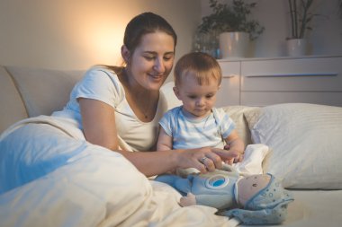 Gülümseyen genç annenin bebeği ile yatağa gece oynuyor.