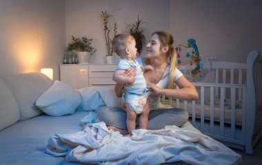 Neşeli bebek çocuk annesiyle yatağa gece oynuyor.