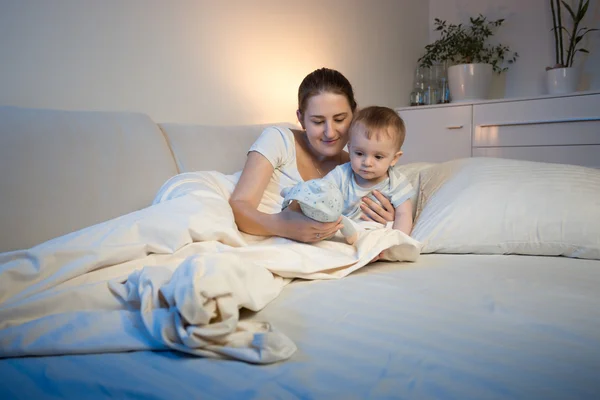 Bebê bonito e sua mãe brincando com brinquedo na cama antes de ir para — Fotografia de Stock