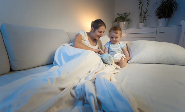 Imagem tonificada da mãe brincando com o bebê na cama à noite — Fotografia de Stock