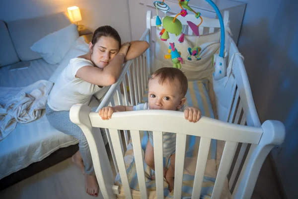 Tired mother got asleep next to baby's crib — Stock Photo, Image