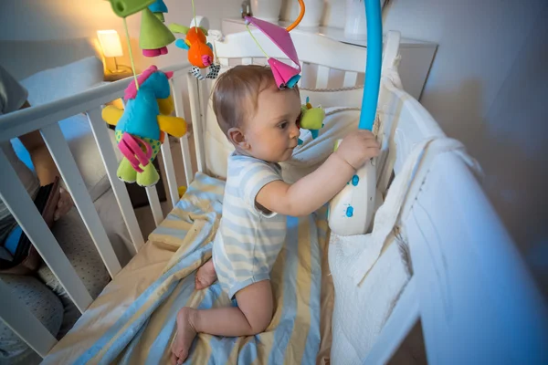 Förtjusande baby pojke stående i babysäng och leker med leksak karusell — Stockfoto
