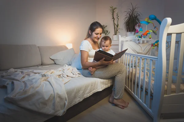 Retrato de mãe segurando bebê menino de joelhos e lendo-lhe um b — Fotografia de Stock