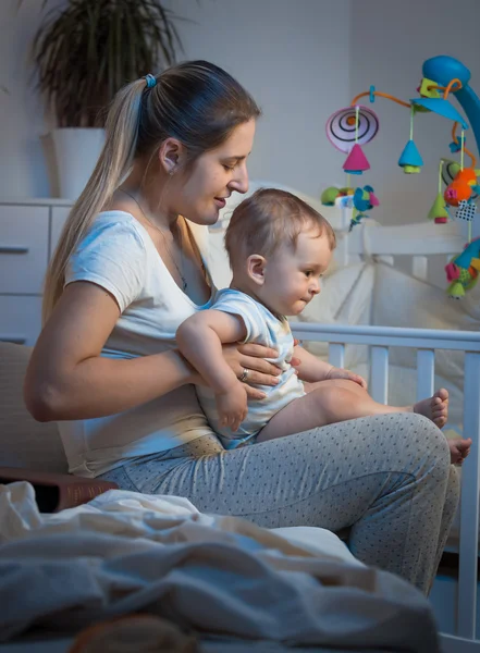 Urocze dziecko siedzi na kolanach matek w sypialni w nocy — Zdjęcie stockowe