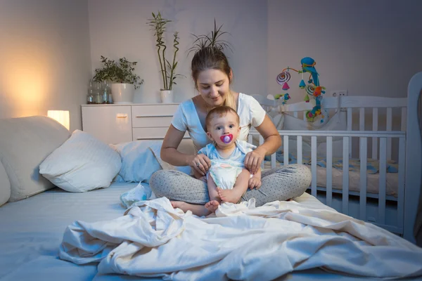 Mother changing diapers to her baby son on bed at night — Stock Photo, Image