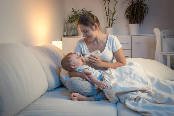 Mladá matka své dítě krmení z láhve v posteli v noci — Stock fotografie