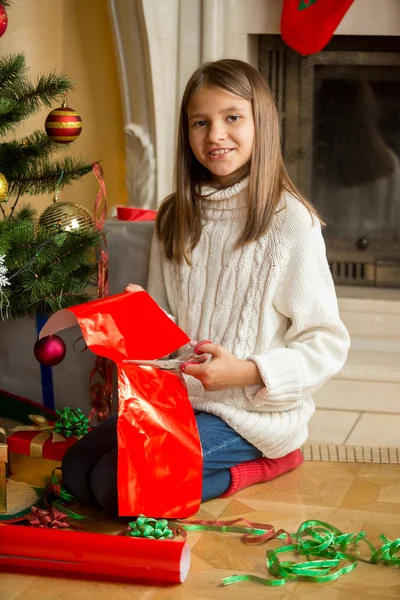 Porträt eines süßen Mädchens, das am Kamin sitzt und Weihnachten einwickelt — Stockfoto