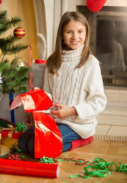 Menina sorridente sentada na árvore de Natal e cortando papel vermelho para — Fotografia de Stock