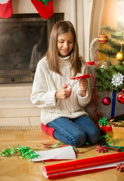 Chica sentada en el árbol de Navidad y cortando copos de nieve de dec —  Fotos de Stock