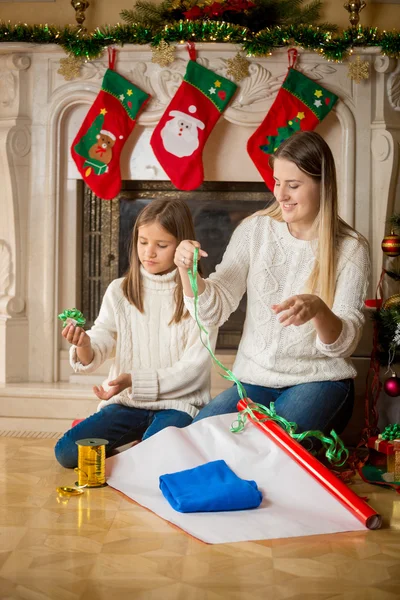 Glückliche Mutter bringt ihrer Tochter bei, wie man ein Weihnachtsgeschenk einwickelt — Stockfoto