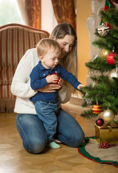 Mãe mostrando seu filho bebê como decorar a árvore de Natal com — Fotografia de Stock