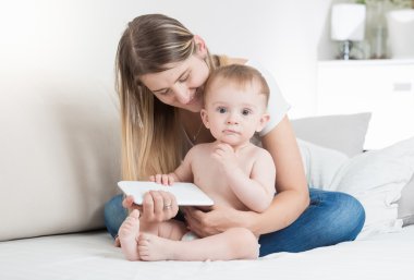 Bebeği ile kanepede oturan ve tablet P kullanma güzel kadın