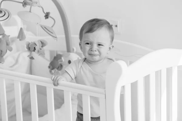 Retrato preto e branco do bebê em pé no berço e chorando — Fotografia de Stock