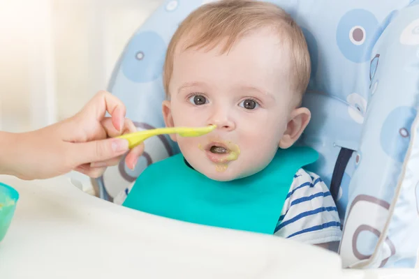 Retrato de adorable bebé en delantal comiendo salsa de frutas de cuchara — Foto de Stock