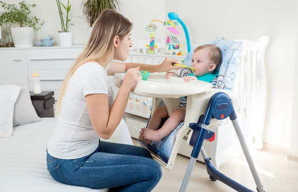 Bella madre che alimenta il suo bambino in seggiolone — Foto Stock