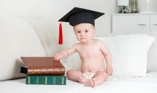 10 Monate altes Baby in Mörtelmütze sitzt mit Stapel Buch — Stockfoto