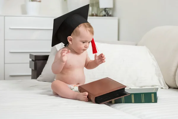 Desnudo bebé chico usando negro graduación gorra mirando stack de — Foto de Stock