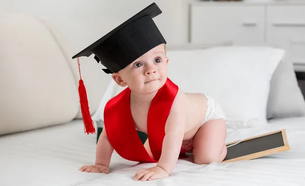 Adorable 10 months old baby in graduation cap crawling on bed — Stock Photo, Image