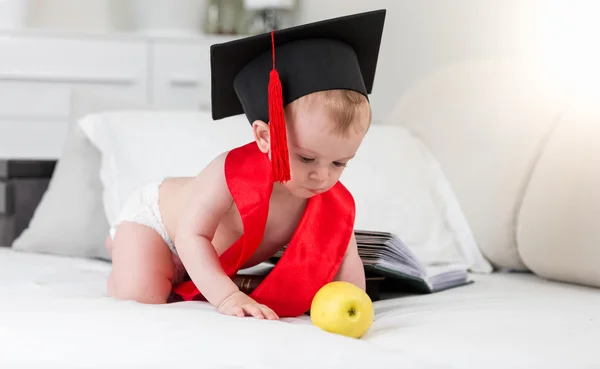 Bebé prodigio en gorra de graduación y cinta alcanzando la manzana — Foto de Stock