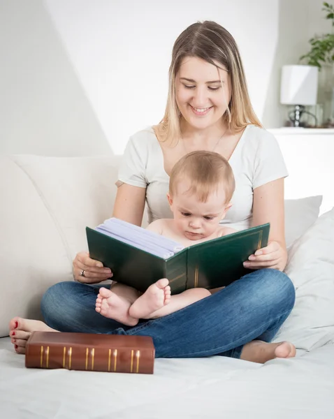 Happymother sentado en el sofá en la sala de estar y libro de lectura a h —  Fotos de Stock