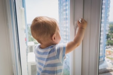 Cute baby boy pulling by the window handle. Concept of child in  clipart
