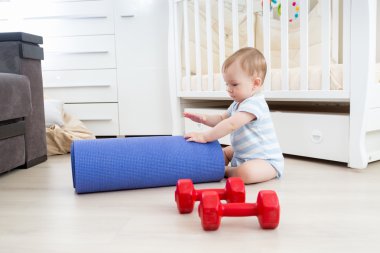 Gülümseyen bebek kattaki fitness mat ve halter ile oynuyor. Co