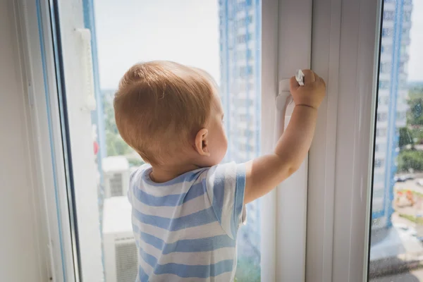 Un bel bambino che tira vicino alla maniglia della finestra. Concetto di bambino in — Foto Stock