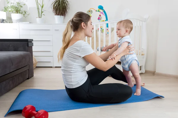 Madre sonriente practicando yoga en la esterilla de fitness en la sala de estar — Foto de Stock