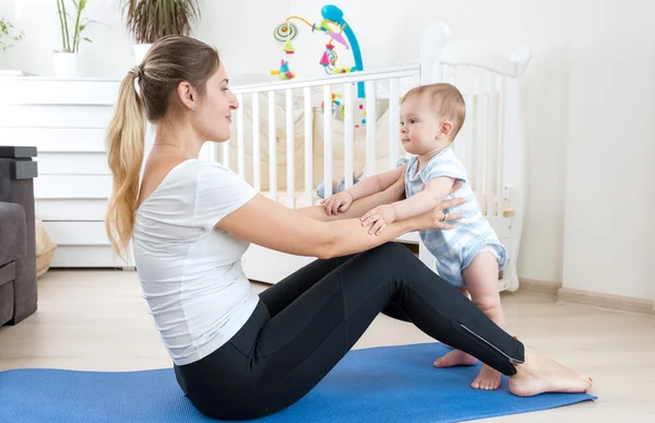 Joven madre estirándose en la alfombra de fitness con su bebé — Foto de Stock