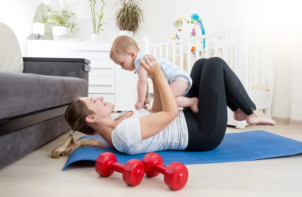 Madre haciendo yoga con su bebé en el suelo en la sala de estar — Foto de Stock